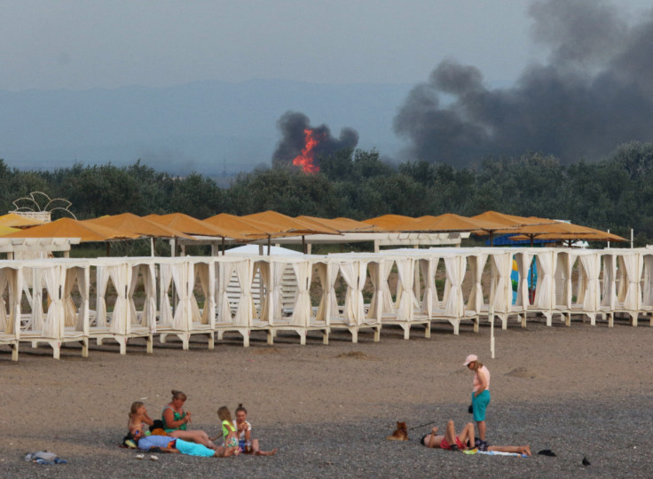 People rest on a beach as smoke and flames rise after explosions at a Russian military airbase, in Novofedorivka