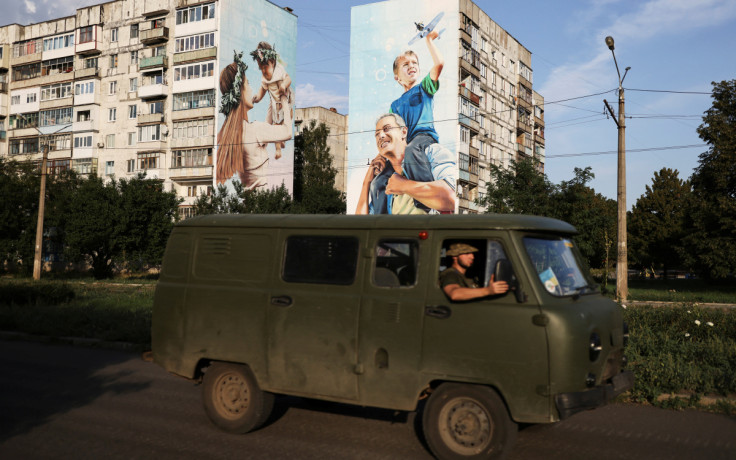 Ukraine servicemen drive past a graffiti of a family painted on damaged buildings in Bakhmut