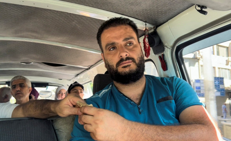 Khaled al-Hassi, a minibus driver, receives money from a customer in Damascus