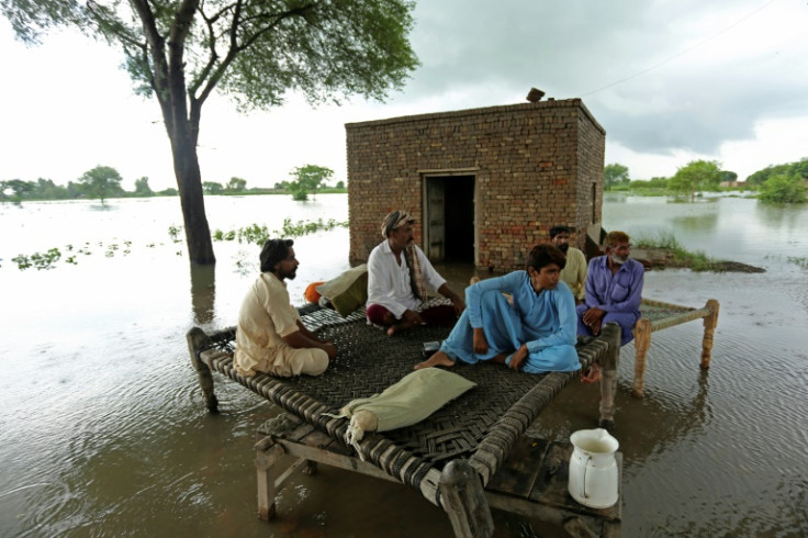 Rural residents sit on a tradional charpai bed in a flooded part of Rajanpur district