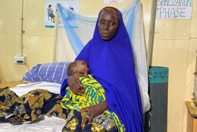 Fatima Usman carries her child, Aisha, as she sits on a bed in a treatment center for severely malnourished children in Damaturu, Yobe