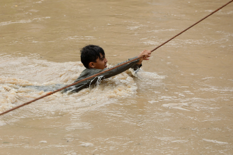 A boy crosses a flooded street, with the help of a wire fastened on both ends, following rains and floods during the monsoon season in Charsadda