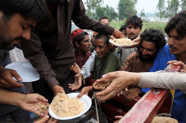Flood victims receive boiled rice from relief workers, after taking refuge on a motorway, following rains and floods during the monsoon season in Charsadda