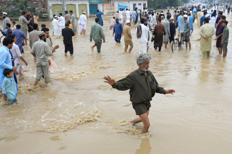 A man balances himself as he, along with others, walks on a flooded road, following rains and floods during the monsoon season in Charsadda