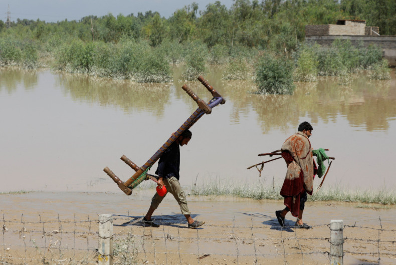 Men walk with their belongings along the flood waters following rains and floods during the monsoon season in Charsadda