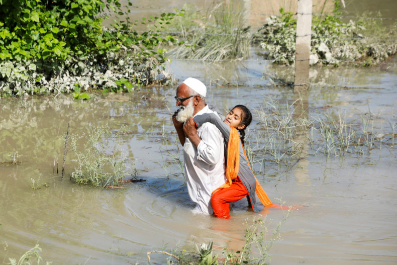 A man wades through flood waters carrying his grand daughter on his back following rains and floods during the monsoon season in Charsadda