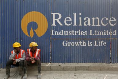 Labourers rest in front of an advertisement of Reliance Industries Limited at a construction site in Mumbai