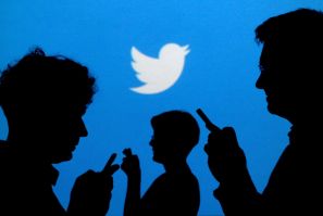 People holding mobile phones are silhouetted against a backdrop projected with the Twitter logo