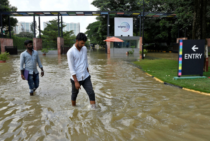 People wade through a waterlogged road in front of the entrance of IT major Wipro Ltd following torrential rains in Bengaluru