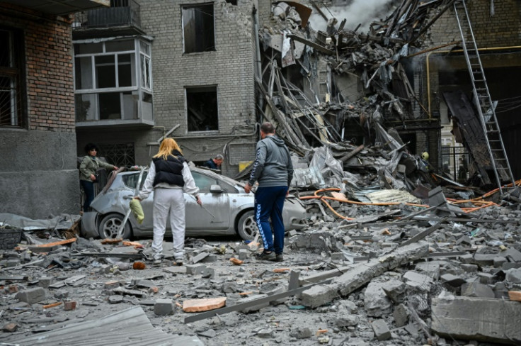 Penduduk setempat berdiri di tengah puing-puing sebuah apartemen setelah terkena serangan rudal Rusia di Kharkiv, Ukraina.