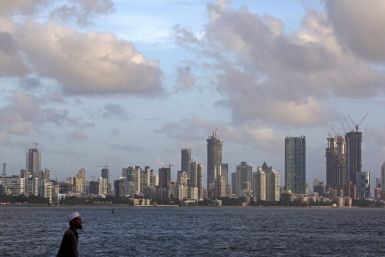 A man walks at the seafront as scattered clouds are seen over Mumbai's skyline
