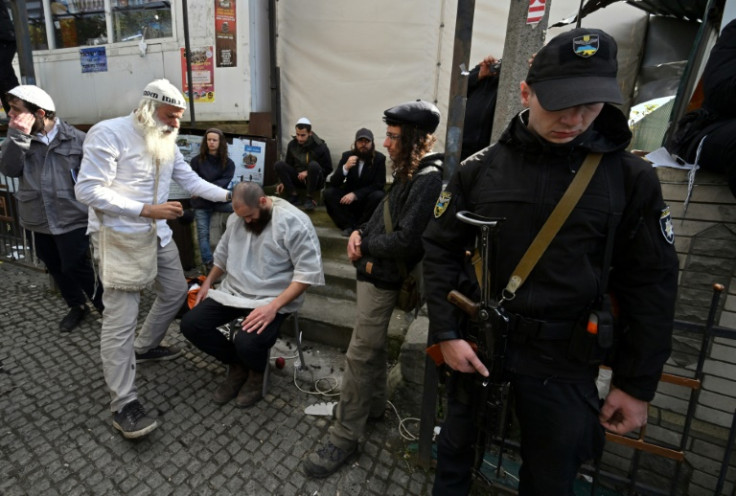 An armed policeman stands guard as Hasidic Jewish pilgrims have their hair cut after praying at the tomb of Rabbi Nachman to mark the Jewish new year