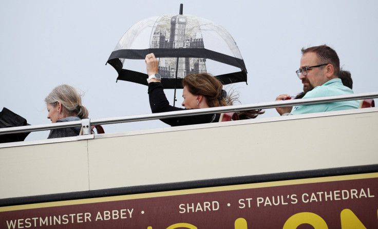 A woman on a tourist bus protects herself from a downpour of rain, in London