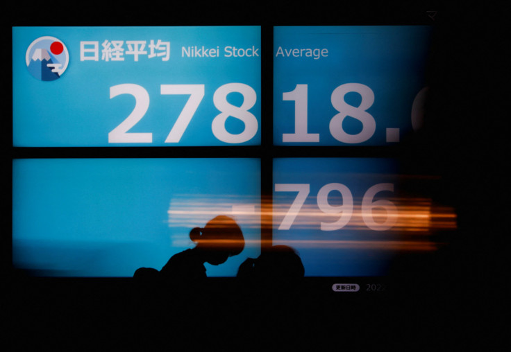 People walk past an electric board showing Japan's Nikkei share average in Tokyo