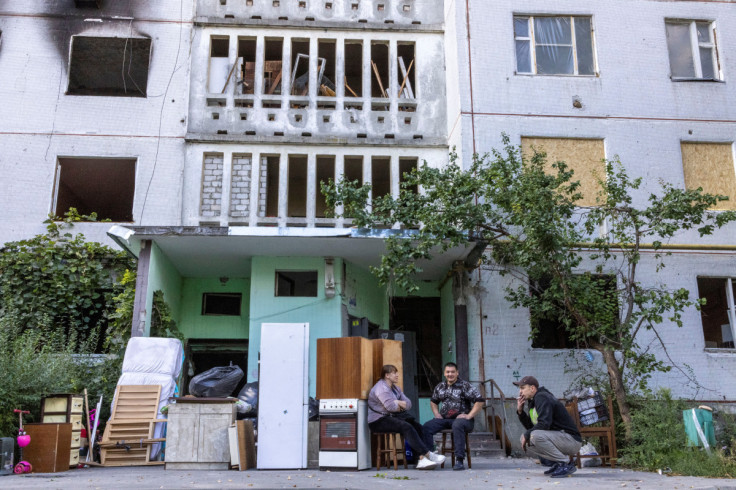 Locals sit next to their belongings from their destroyed apartment, as they wait for the rented vehicle for transport, in Saltivka neighbourhood of Kharkiv