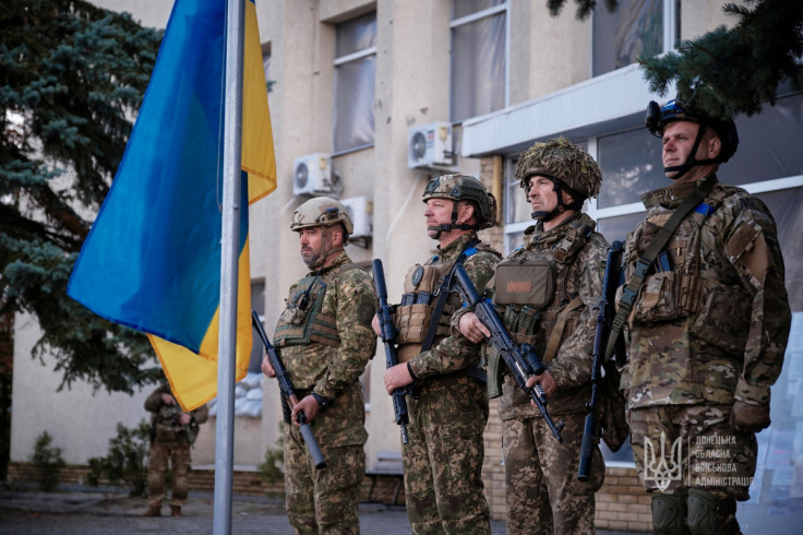 Ukrainian service members attend a flag raising ceremony in the town of Lyman