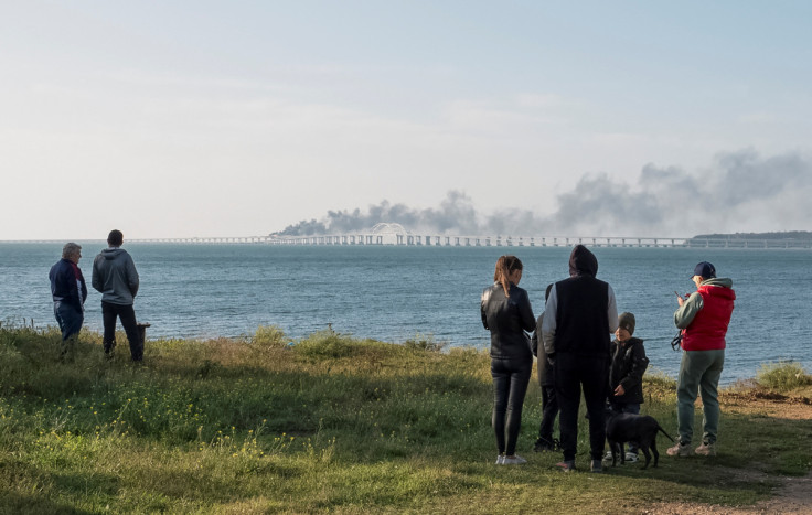 People watch fuel tanks ablaze and damaged sections of the Kerch bridge in the Kerch Strait, Crimea