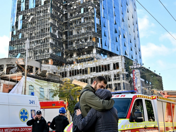 People comfort each other outside a partially destroyed office building after several Russian strikes hit the Ukrainian capital