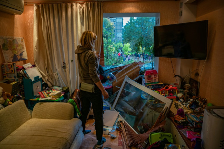 A woman looks out of a broken window of a damaged apartment