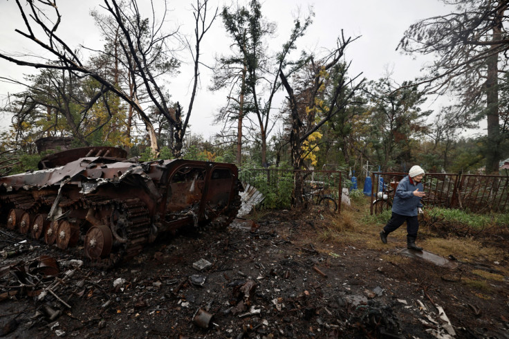 Raiisa, 71, who said she was preparing the grave to bury her husband who died of illness during the Russian occupation of her town, walks out the cemetery  past a destroyed Russian armoured vehicle, in Sviatohirsk