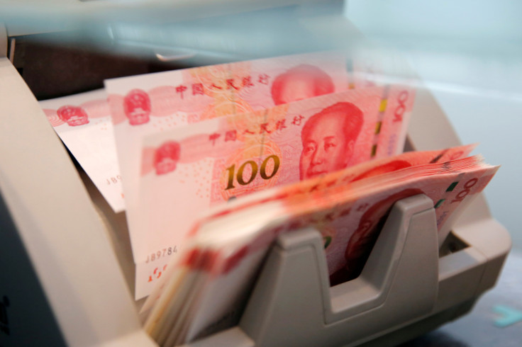 Chinese 100 yuan banknotes are seen in a counting machine while a clerk counts them at a branch of a commercial bank in Beijing