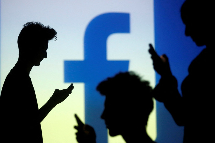 People pose with mobile devices in front of projection of Facebook logo in this picture illustration taken in Zenica