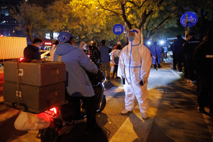 A pandemic prevention worker in a protective suits keeps watch on people lining up to get swab tests at a testing booth as outbreaks of COVID-19 continue in Beijing