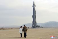KCNA photos show Kim holding hands with a girl in a white jacket and red shoes, walking in front of a giant missile