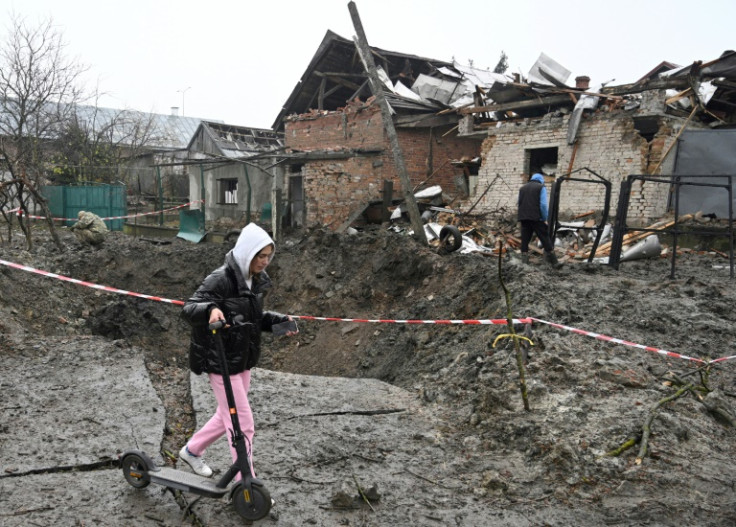 A girl walks her scooter past a crater after a Russian missile strike in a village near the western Ukrainian city of Lviv