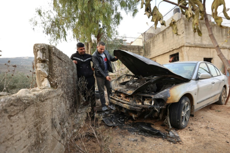 Palestinian men inspect a burned out car which they said it was set ablaze by Israeli settlers overnight