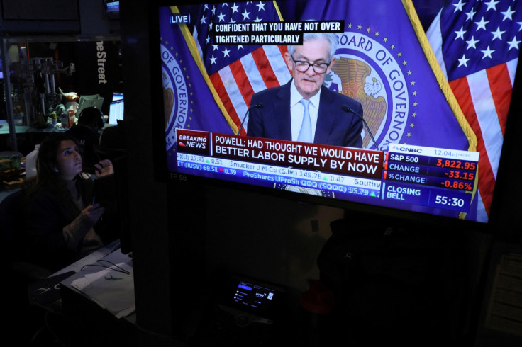 A screen displays Federal Reserve Chair Powell speaking as a trader works on the floor of the NYSE in New York