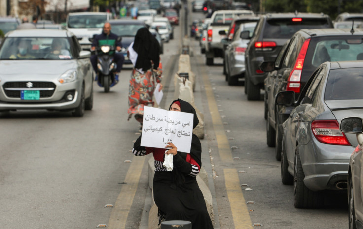 A beggar holds a sign reading "My mother is sick with cancer, she needs chemotherapy", in Sidon