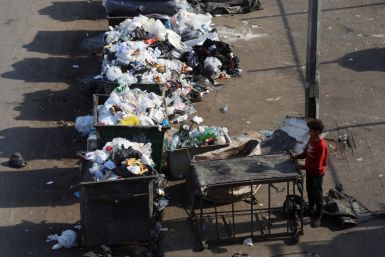 A boy stands near a dumpster, in Beirut