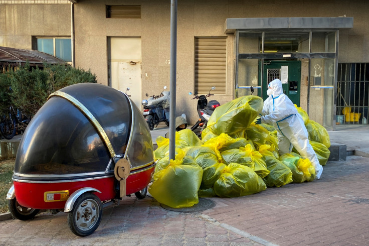 A pandemic prevention worker in a protective suit piles up bags of medical waste outside a building in Beijing