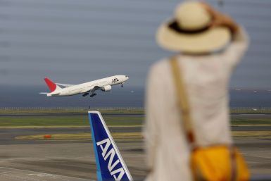 Woman watches a JAL aeroplane taking off behind an ANA aeroplane at Haneda airport in Tokyo