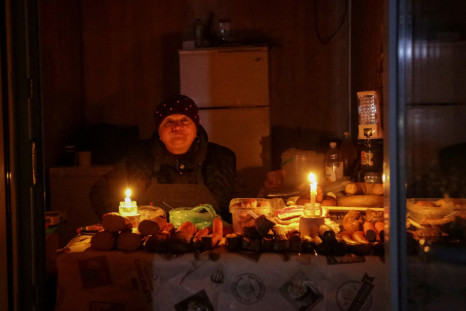 A vendor waits for customers in a small store, lit with candles during a power outage, after critical civil infrastructure was hit by Russian missile attacks in Odesa