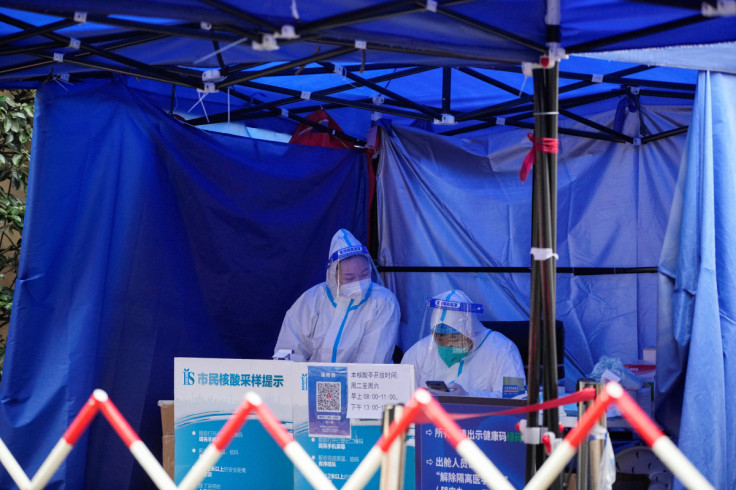 Workers in protective suits wait for people at a nucleic acid testing site in Shanghai