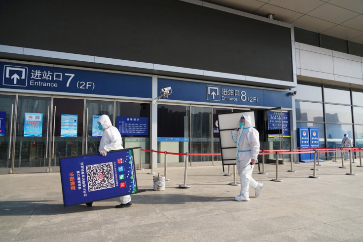 Workers in protective suits remove signs of a health code after the government withdrew this measure, at an entrance of a railway station in Xining