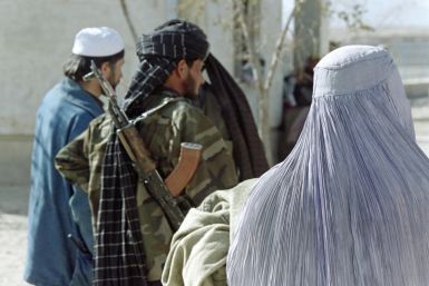 An Afghan woman, wearing the Taliban-imposed burqa, waits near a militiaman, in November 1996, to receive a blanket, a quilt and warm clothes from aid workers as part of a UN winter relief distribution program
