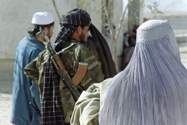 An Afghan woman, wearing the Taliban-imposed burqa, waits near a militiaman, in November 1996, to receive a blanket, a quilt and warm clothes from aid workers as part of a UN winter relief distribution program