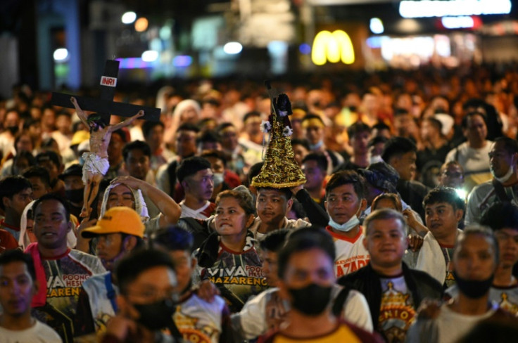 Roman Catholic devotees, some carrying miniature statues of the Black Nazarene, walk along a street during the "walk of faith" as they celebrate the annual feast of the Black Nazarene in Manila on January 8, 2023