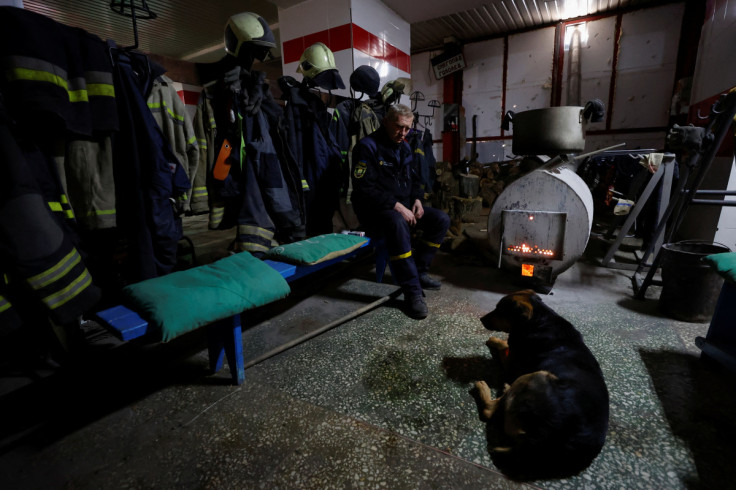 A rescuer and a dog warm up next to a wood stove inside a State Emergency Service station in the town of Bakhmut