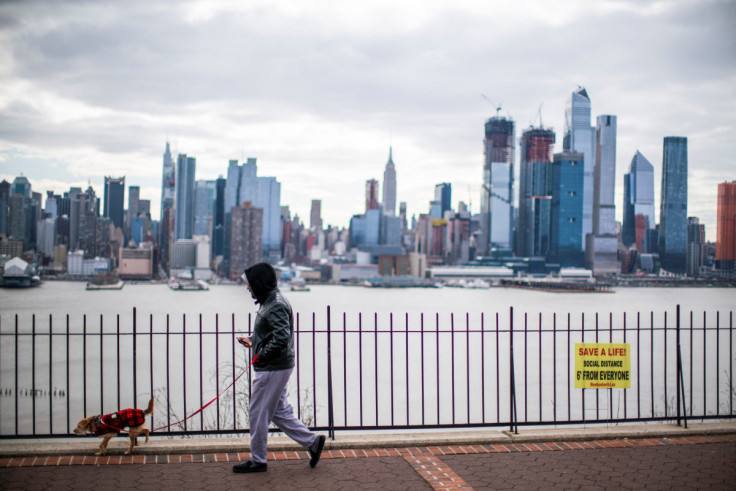 A man walks his dog without wearing a face mask during the coronavirus disease (COVID-19) pandemic, while the Empire State Building and New York skyline are seen from Weehawken, New Jersey