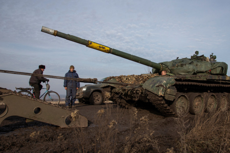Ukrainian serviceman looks on and a local resident rides a bicycle while a broken tank is pulled to a truck near the frontline town of Bakhmut