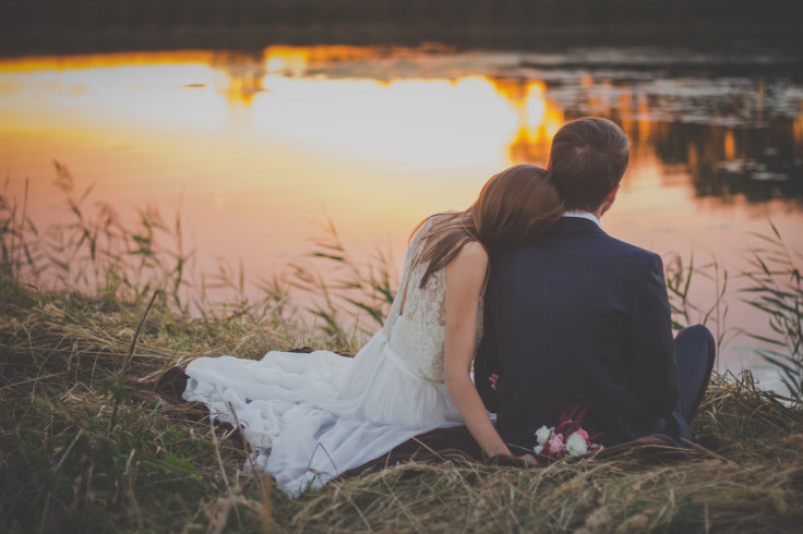 Bride and groom sit by pond