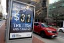 Car drives next to a board at a bus stop showing a U.S. national debt figure in Washington