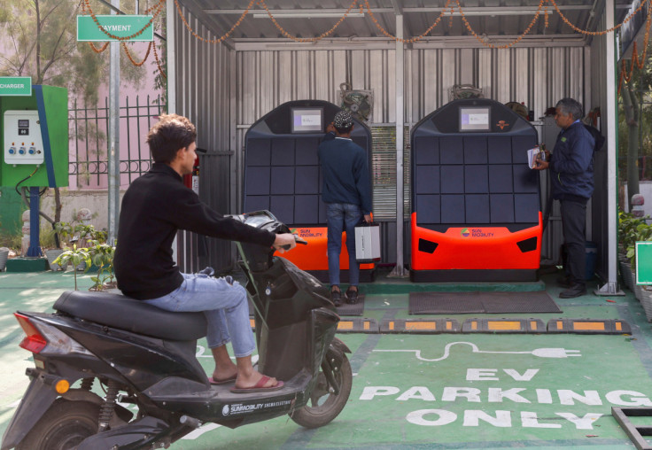 A man sits on his electric scooter as he waits to swap his battery at a Sun Mobility battery swapping station in New Delhi