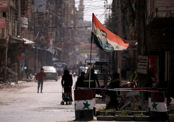 A national flag depicting a picture of Syria's President Bashar al-Assad flutters at a checkpoint in Douma