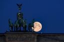 An almost full moon is seen behind the quadriga of Brandenburg Gate in Berlin