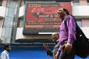 Pedestrians walk past a screen displaying news on the Adani Group at the Bombay Stock Exchange